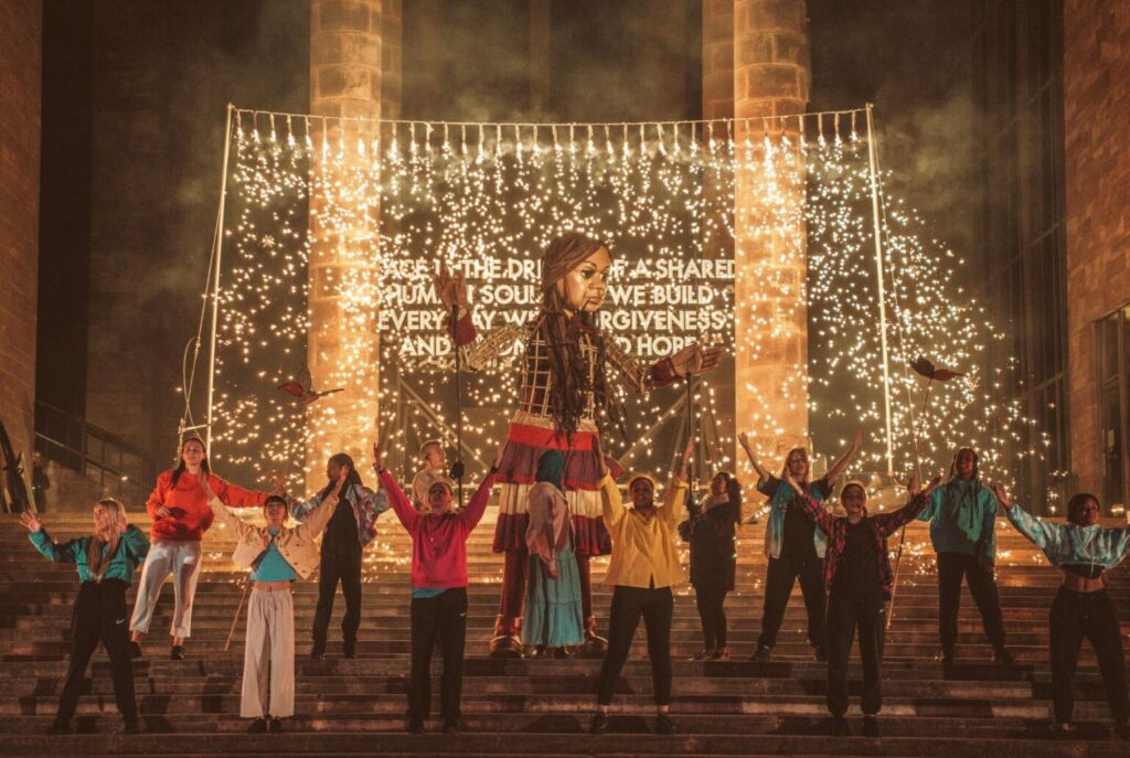 Little Amal and performers outside Coventry Cathedral at night