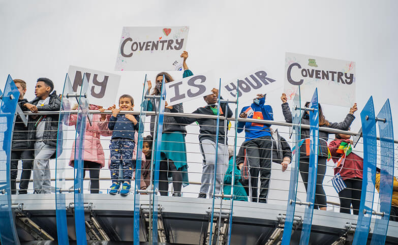 Children standing on a bridge with posters saying My Coventry is your Coventry