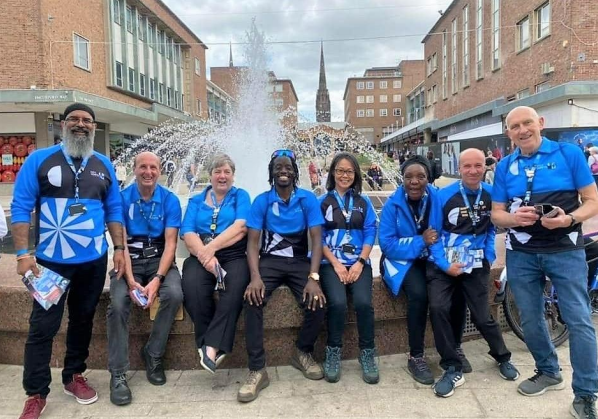 Group of City Host volunteers sitting by a fountain in Coventry city centre.